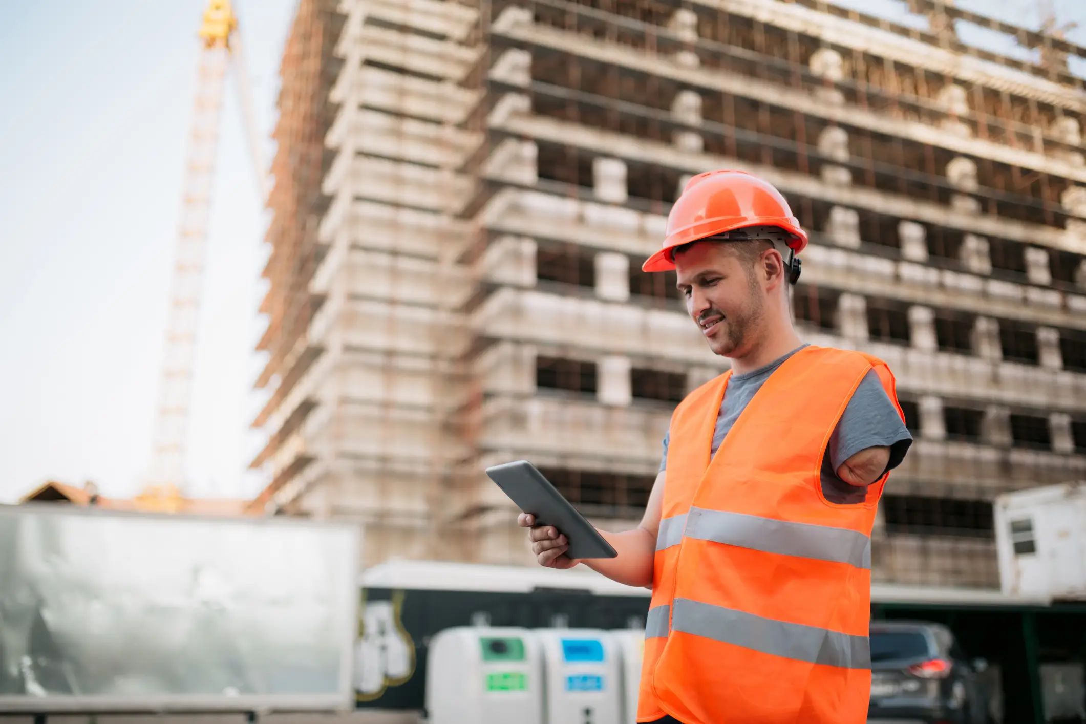 A man in an orange vest and hard hat holding a tablet.